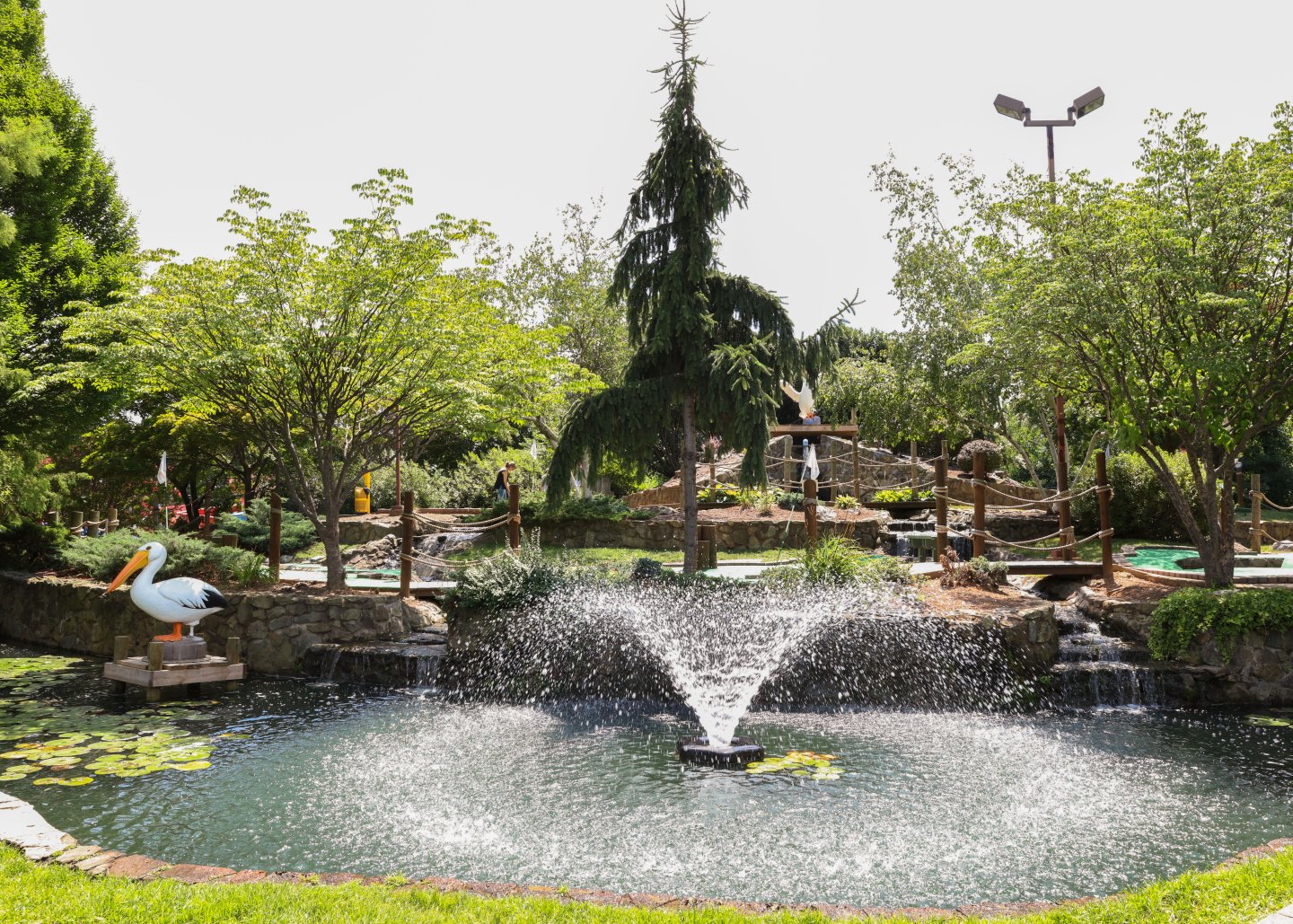 Scenic green space with a fountain, lush greenery, and decorative bird statues.