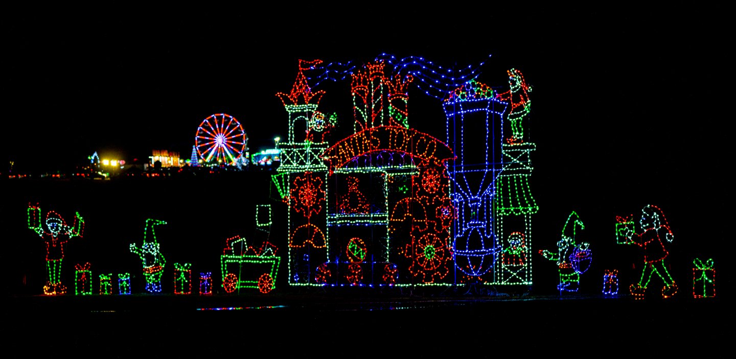 A colorful Christmas light display with Santa, elves, and presents against a dark background.