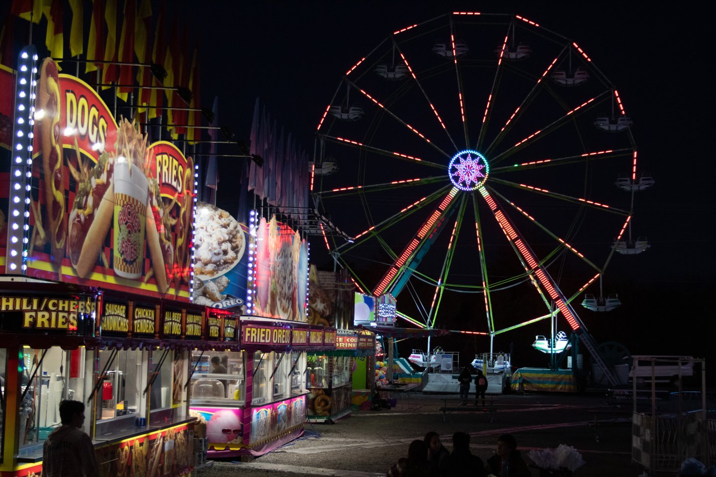 Carnival at night with a lit Ferris wheel and colorful booths.