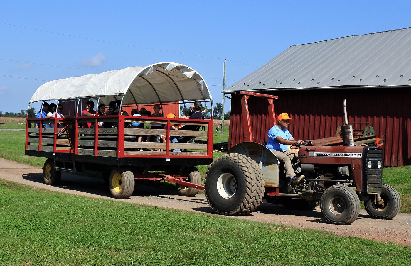Tractor pulling a covered wagon with people on a farm path.