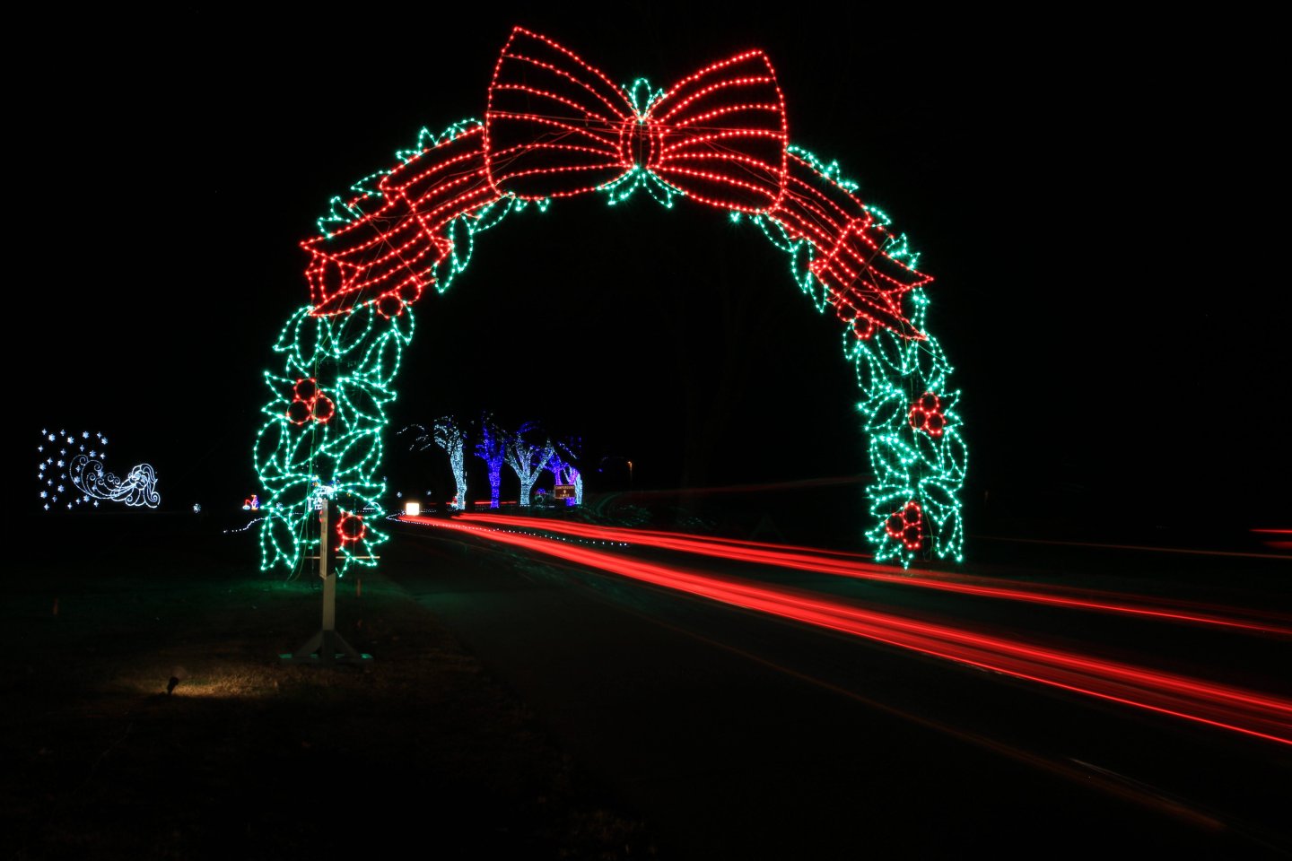 Festive arch of red and green lights with trailing car light streaks.