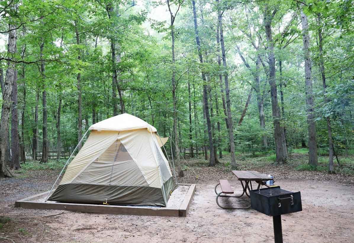 off white tent pitched at a campsite at Bull Run Regional Park with a picnic table and grill