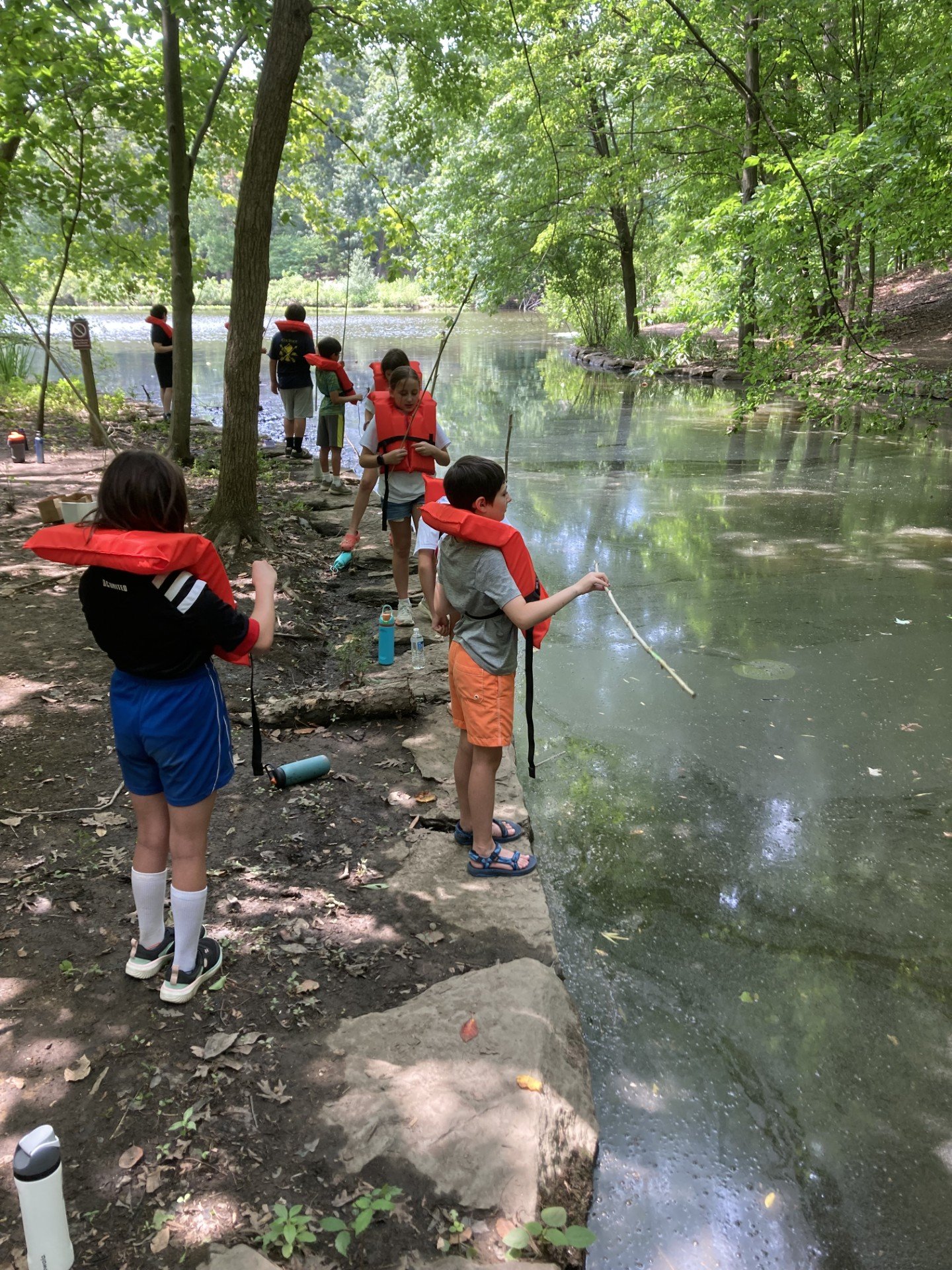Campers at Camp Winkler with life jackets on fishing on the edge of a pond