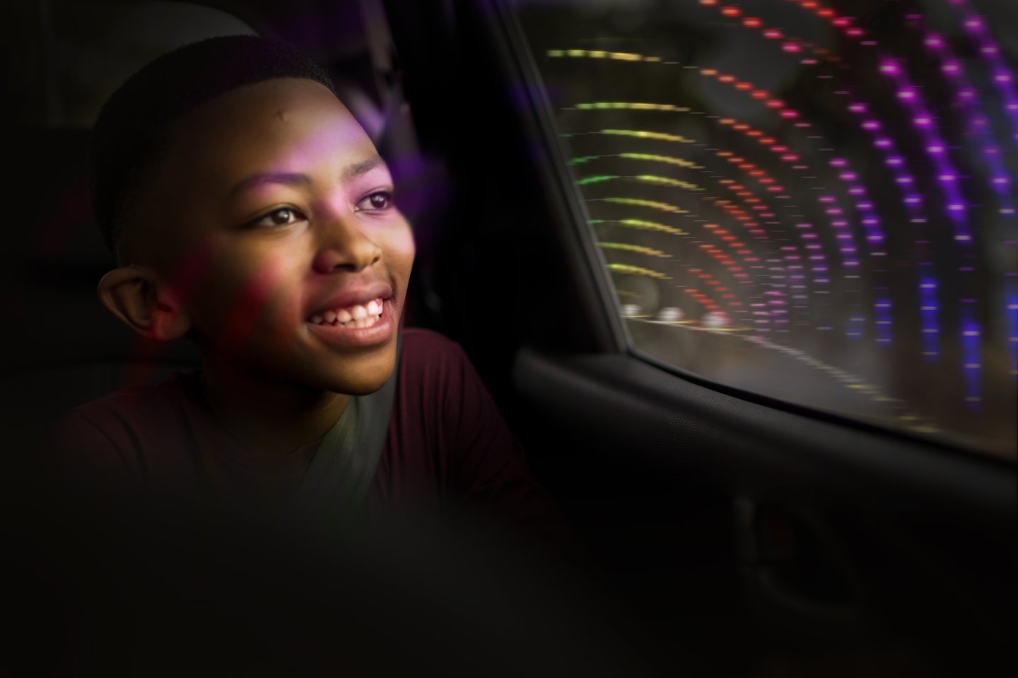 Smiling child looks at colorful lights through car window.