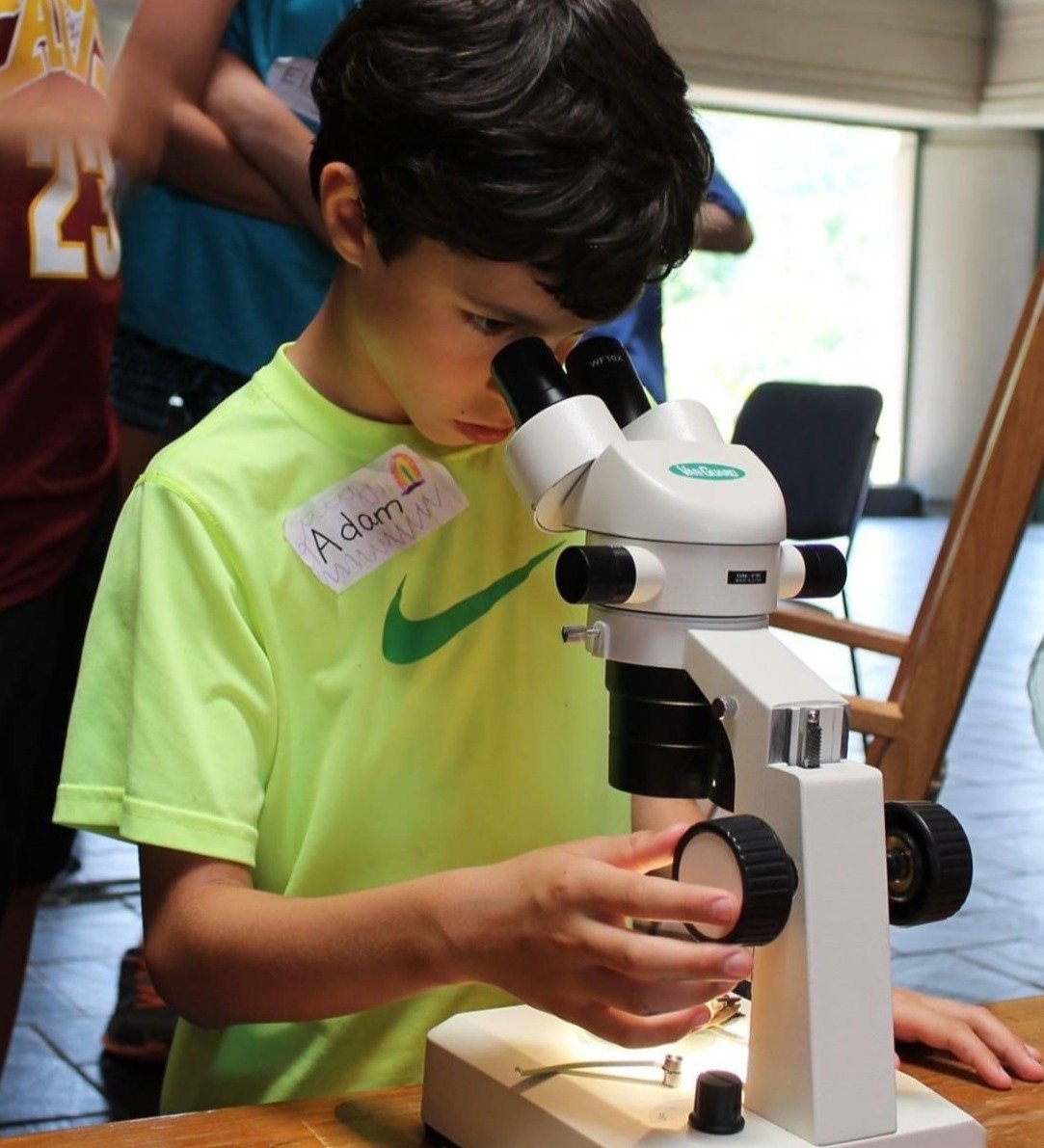 Young boy in a bright shirt looks through a microscope intently.