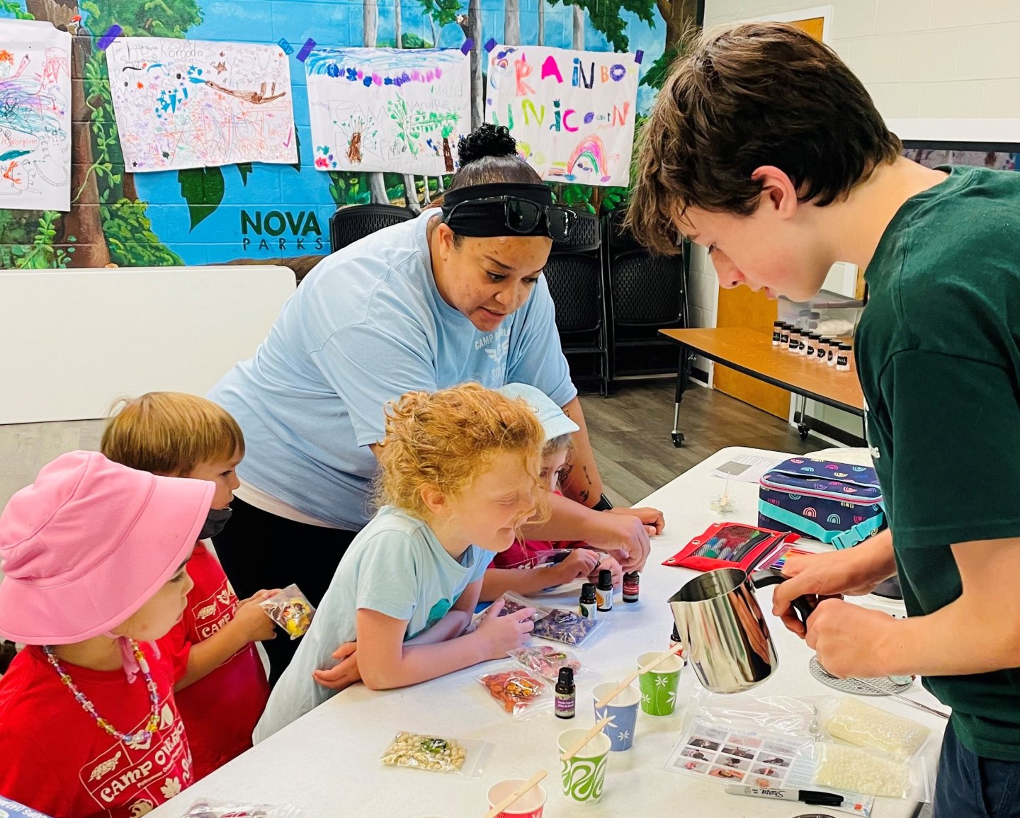 Children and adults engaged in a craft activity at a table with colorful art on walls.